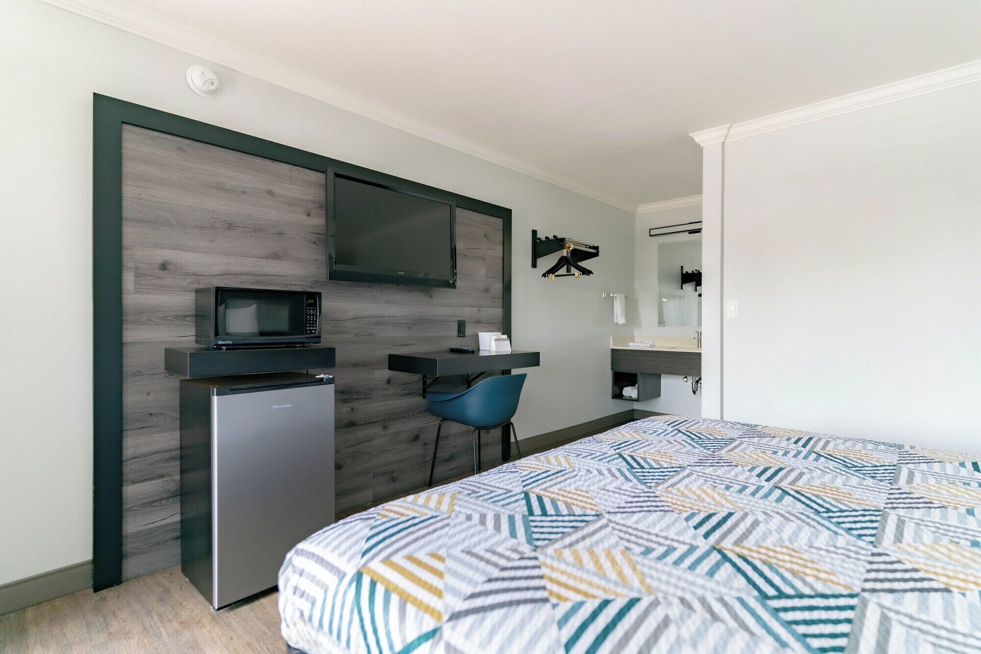 A compact hotel room with a bed, a desk, a microwave, and a small refrigerator.