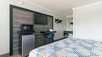 A compact hotel room with a bed, a desk, a microwave, and a small refrigerator.