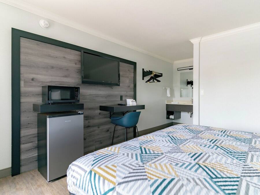 A compact hotel room with a bed, a desk, a microwave, and a small refrigerator.