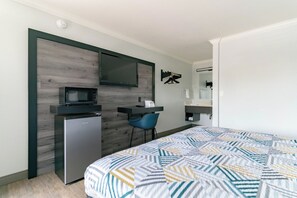 A compact hotel room with a bed, a desk, a microwave, and a small refrigerator. - Motel 6 Pico Rivera, CA - Los Angeles (Pico Rivera)