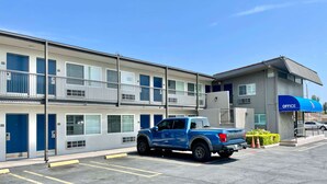 A multi-story motel with numbered rooms, a parking lot, and a blue pickup truck parked in front. - Motel 6 Pico Rivera, CA - Los Angeles (Pico Rivera)