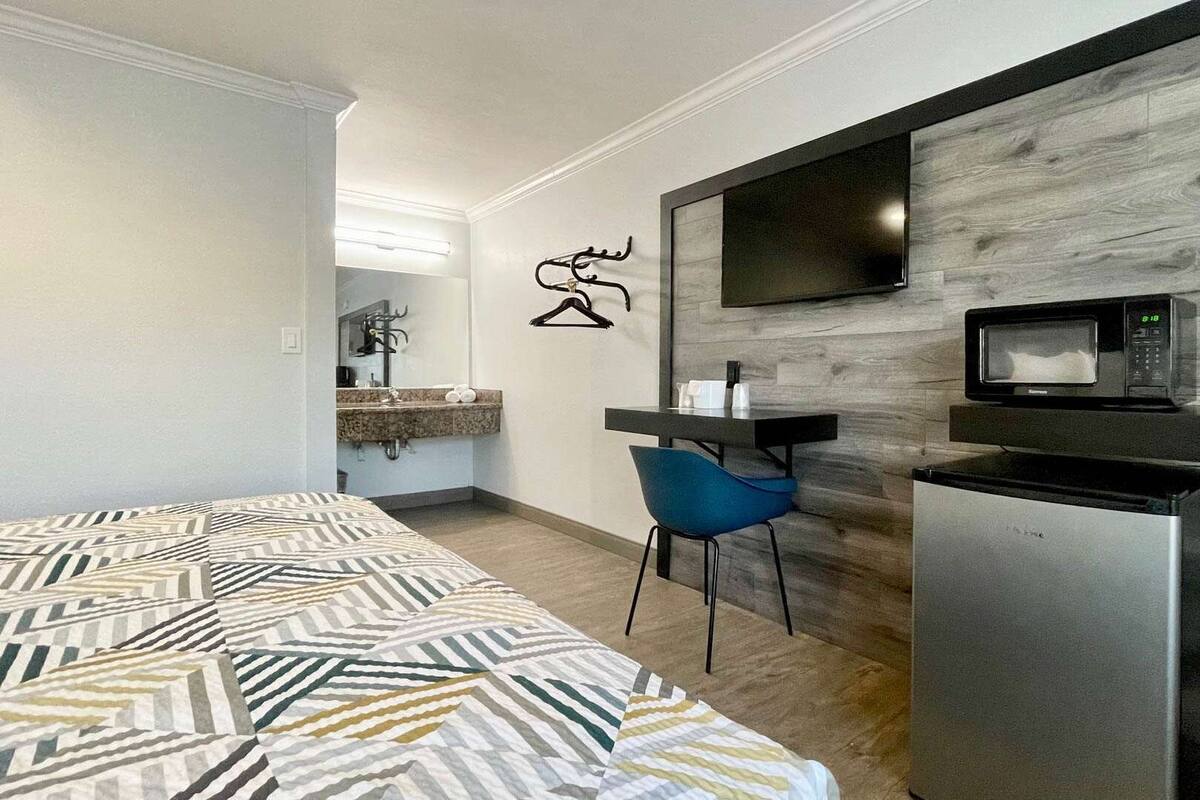 A hotel room with a bed, a desk, a chair, a TV, and a microwave.