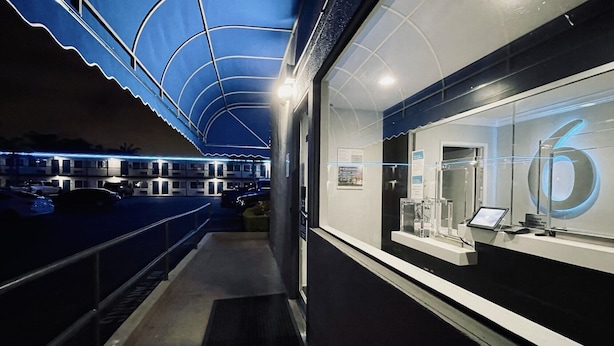 A modern hotel corridor with a glass display case on the right and a blue-lit canopy overhead. - Motel 6 Pico Rivera, CA - Los Angeles (Pico Rivera)