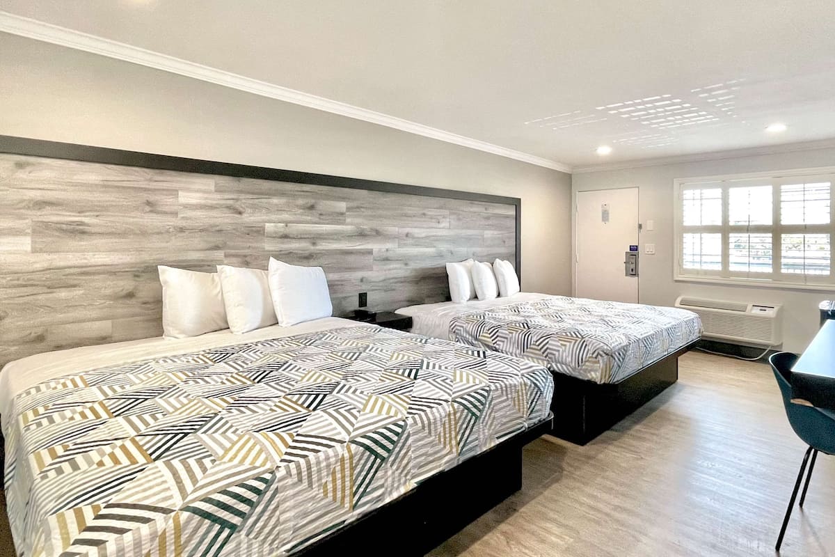 A hotel room with two beds, a desk, and a chair.