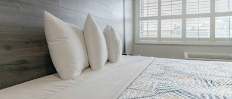 A bedroom with a wooden headboard, a large window with blinds, and a patterned bedspread.