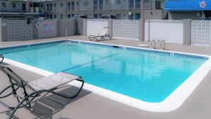 A rectangular swimming pool with a white edge, surrounded by lounge chairs and a covered area. - Motel 6 Pico Rivera, CA - Los Angeles (Pico Rivera)