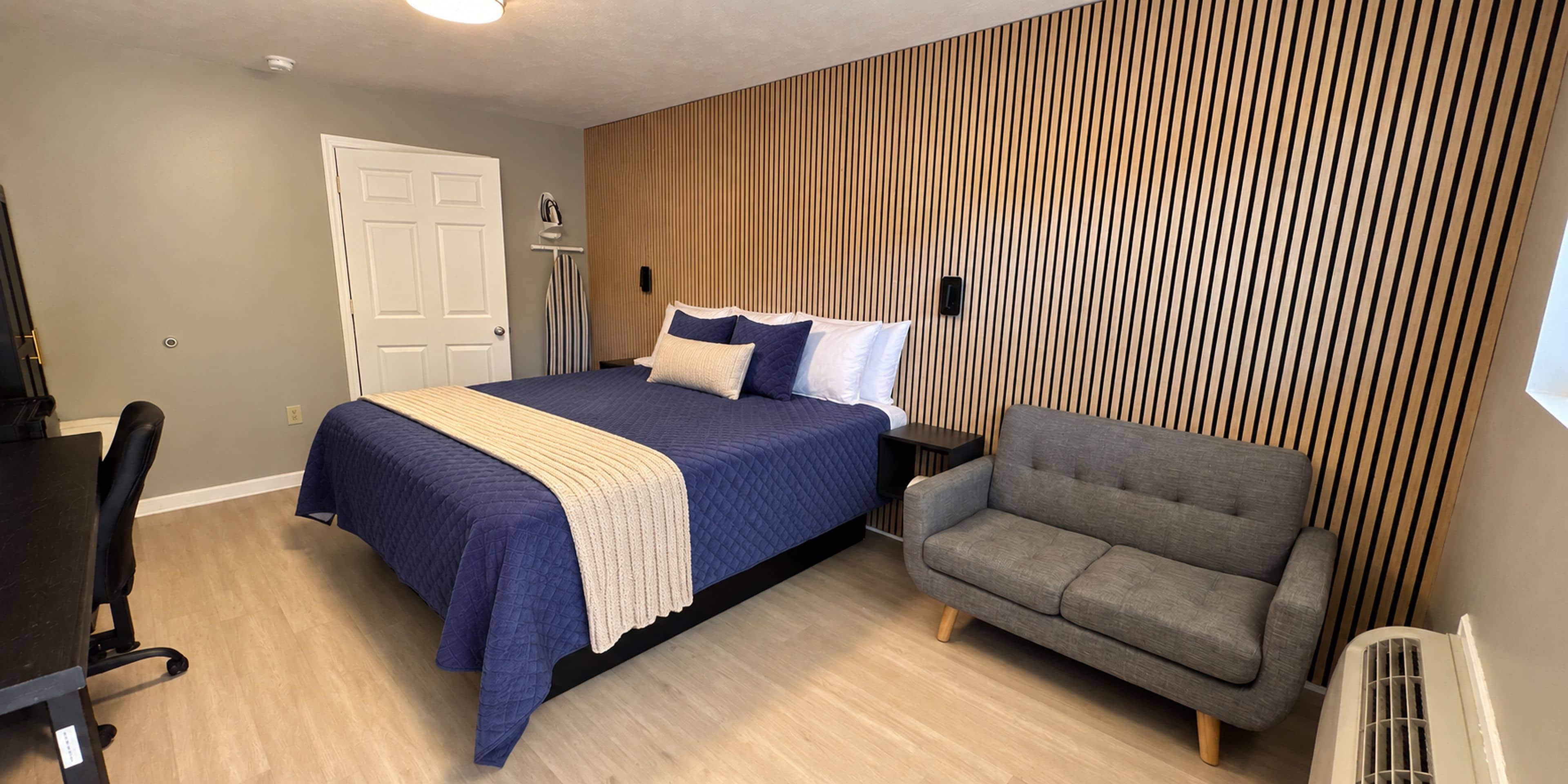 Une chambre moderne avec un lit, un fauteuil gris, un bureau et un mur avec des lambris en bois.