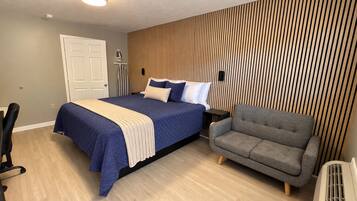 Une chambre moderne avec un lit, un fauteuil gris, un bureau et un mur avec des lambris en bois.