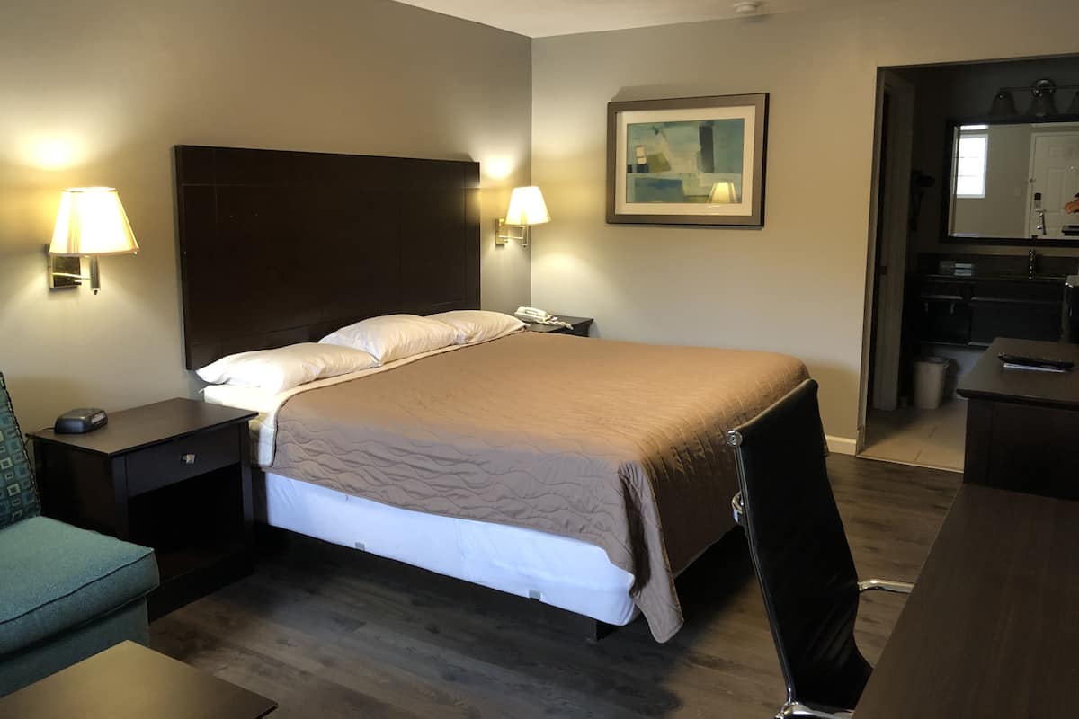 Ein Hotelzimmer mit Bett, Nachttischlampen, einem Nachttisch, einem Schreibtisch und einer kleinen Küchenzeile.