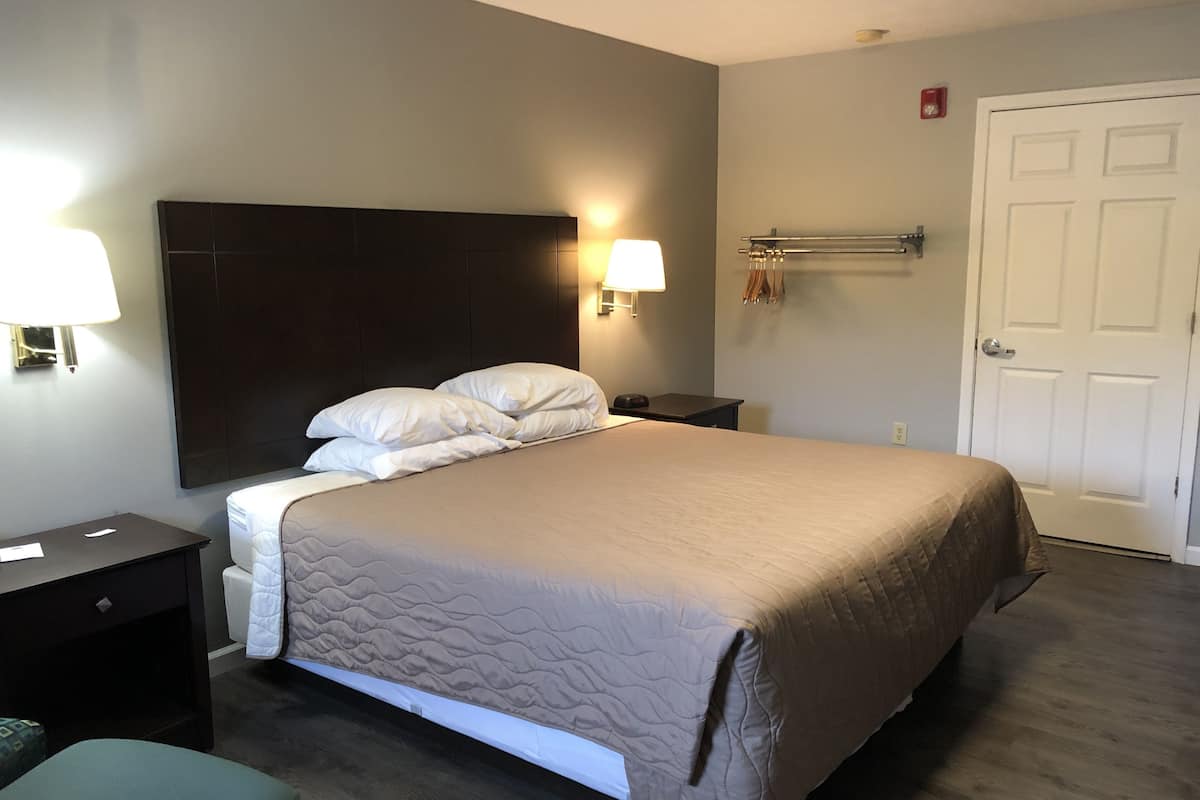 Ein Hotelzimmer mit Bett, Nachttischlampen, einem Nachttisch, einem Stuhl und einer Tür.