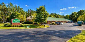 A Deerfield Inn with a green sign, a brick building, and a parking lot with cars. - Deerfield Inn & Suites (Fairview)
