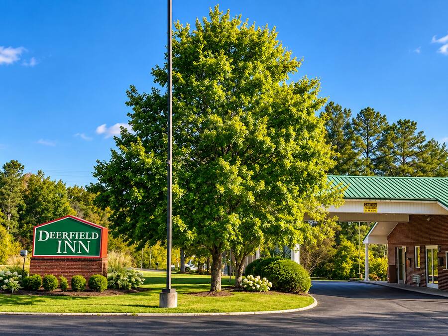 Deerfield Inn mit einem grünen Schild, einem überdachten Parkbereich und einem gepflegten Rasen.