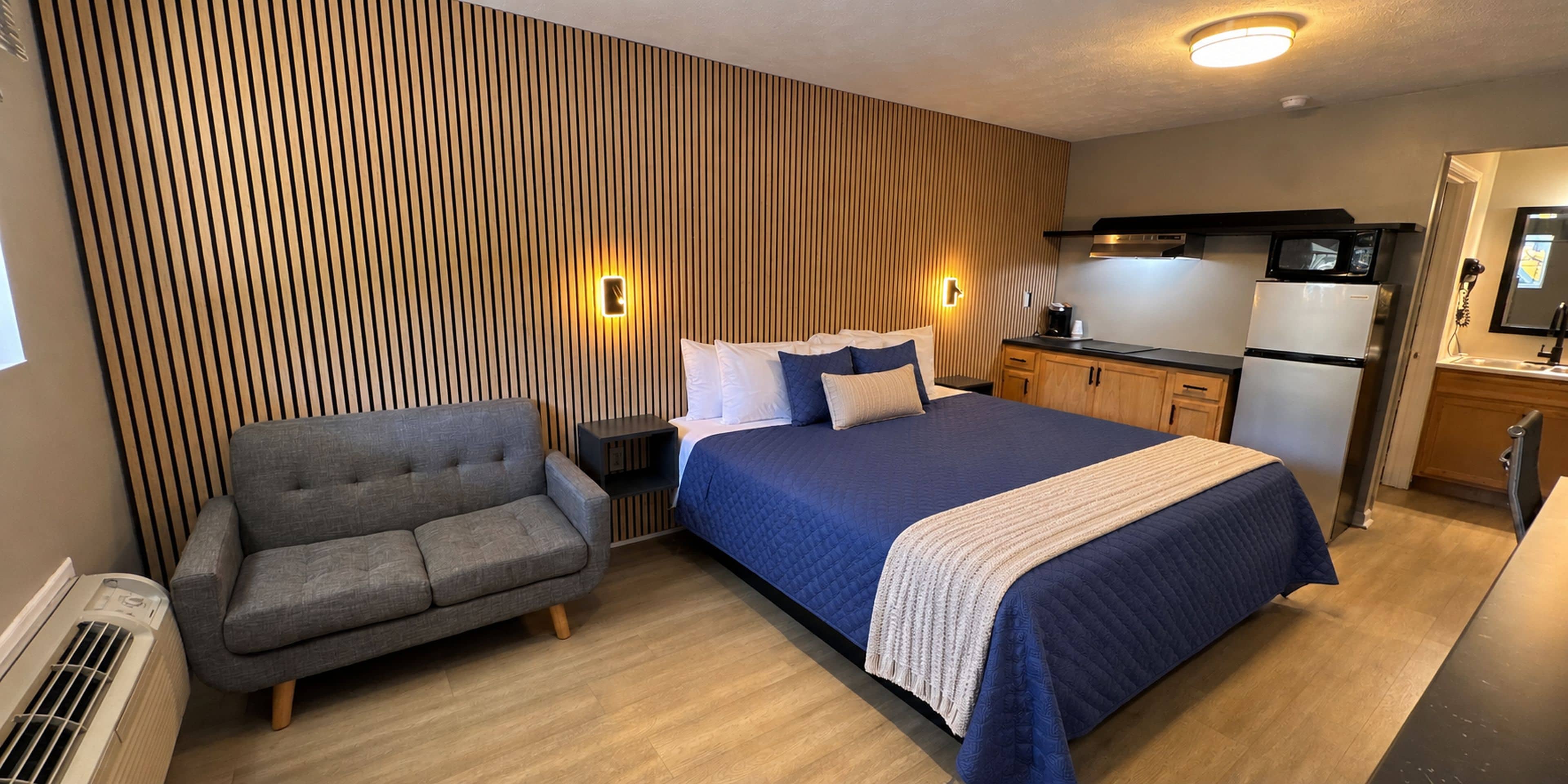 Una habitación de hotel con cama, sofá, kitchenette y pared con líneas verticales.