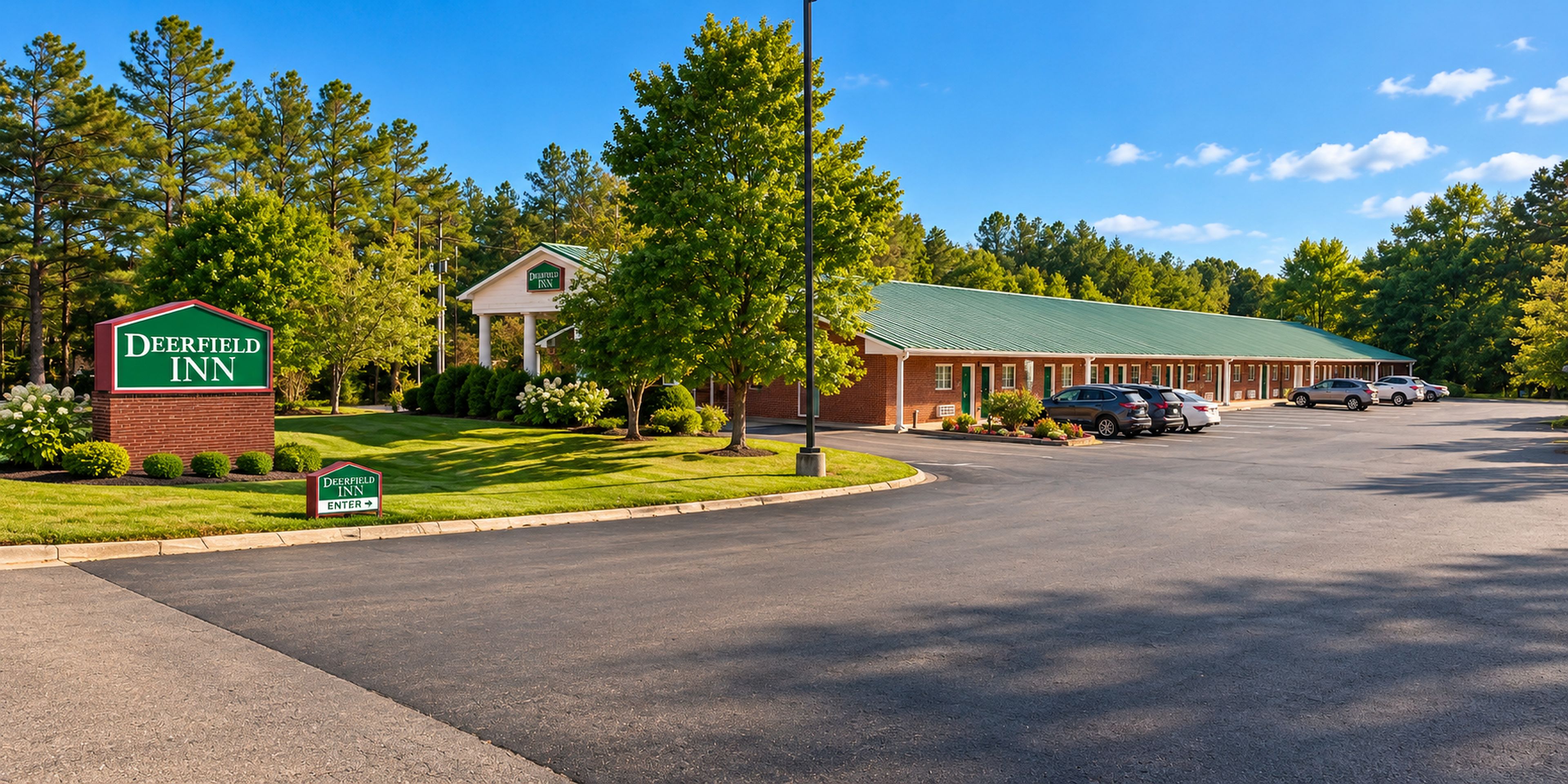 El Deerfield Inn, con un letrero verde, un estacionamiento y un edificio con techo verde.