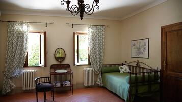 Una habitación con cama, una silla, una mesa con espejo y un radiador.