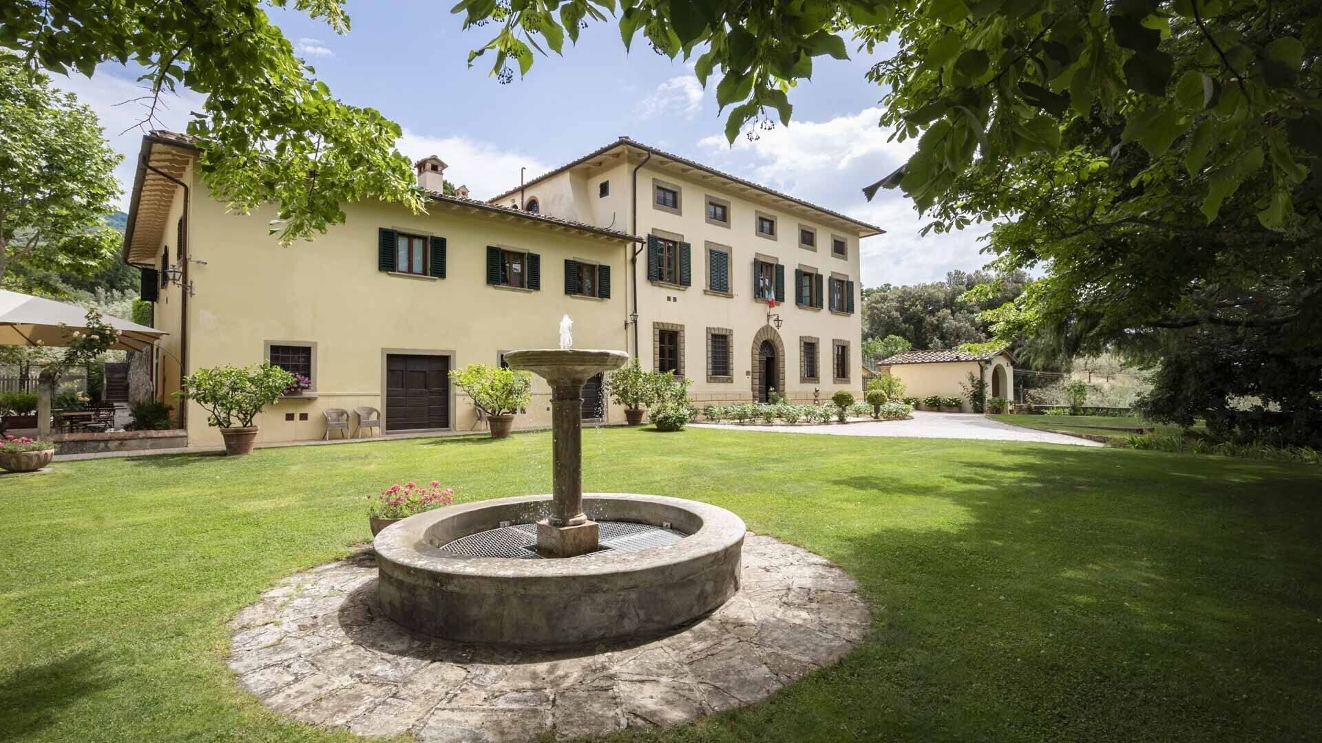 A courtyard with a fountain, a building with multiple windows, and a well-maintained lawn.