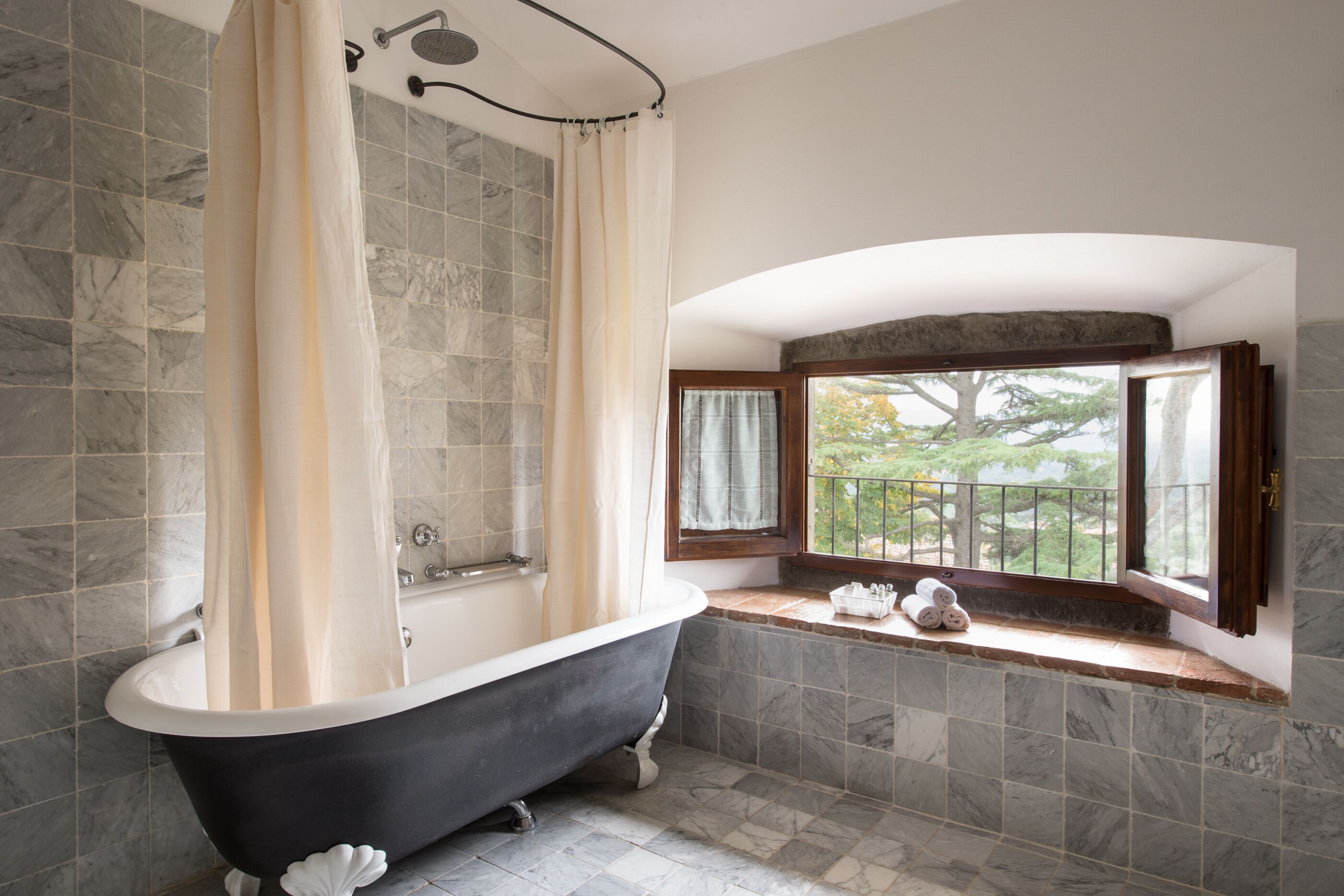 Une salle de bain avec une baignoire sur pieds, des murs carrelés, une fenêtre avec vue et un espace douche.