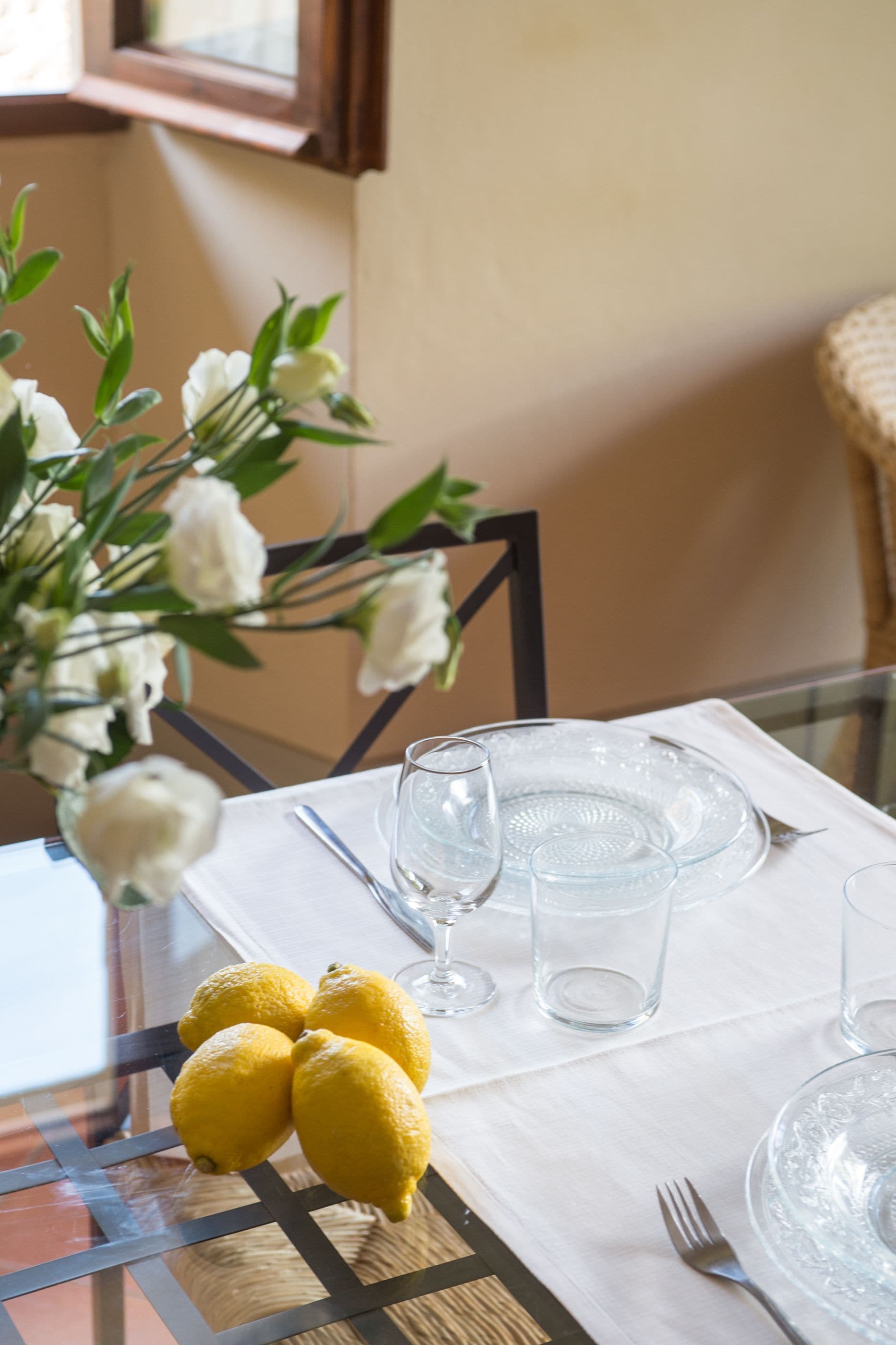 A dining table set with clear glassware and a vase of white flowers.