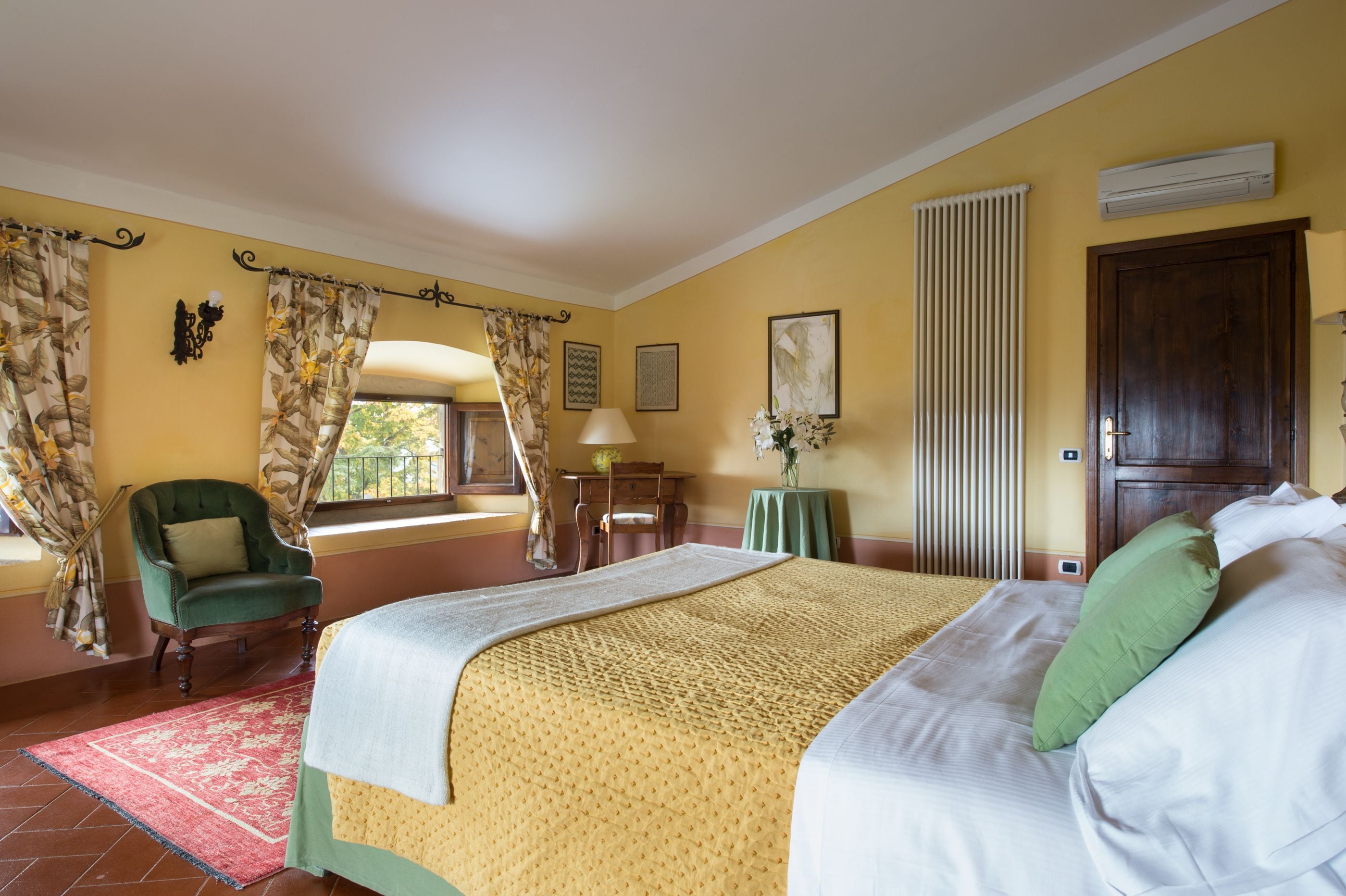 Una habitación de hotel con una cama, una silla, una mesa, una lámpara y un ventanal con cortinas.