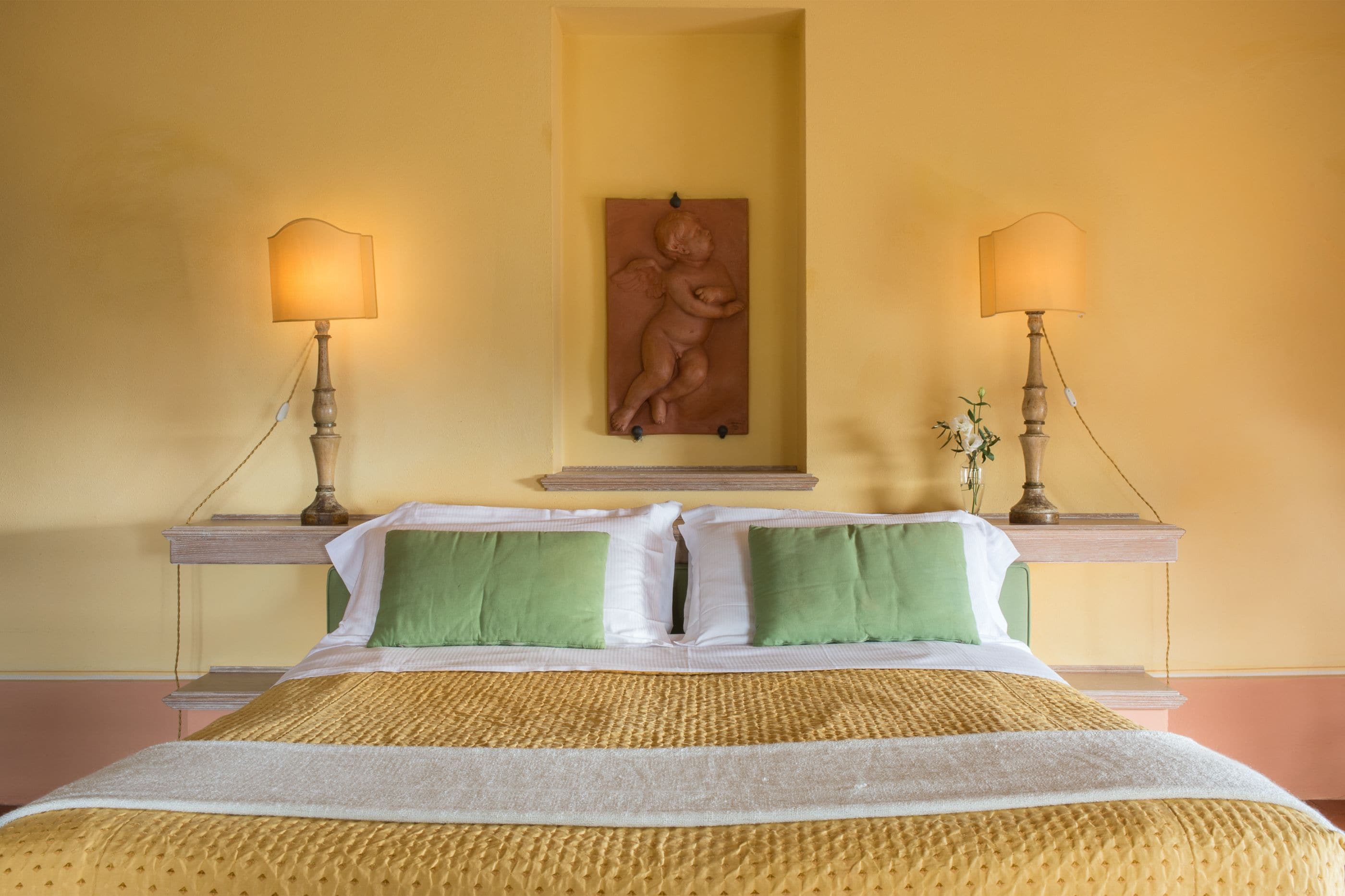 Une chambre d’hôtel avec un grand lit, deux lampes de chevet, un ensemble d’oreillers verts et blancs, une couvre-lit à motifs et une sculpture murale.
