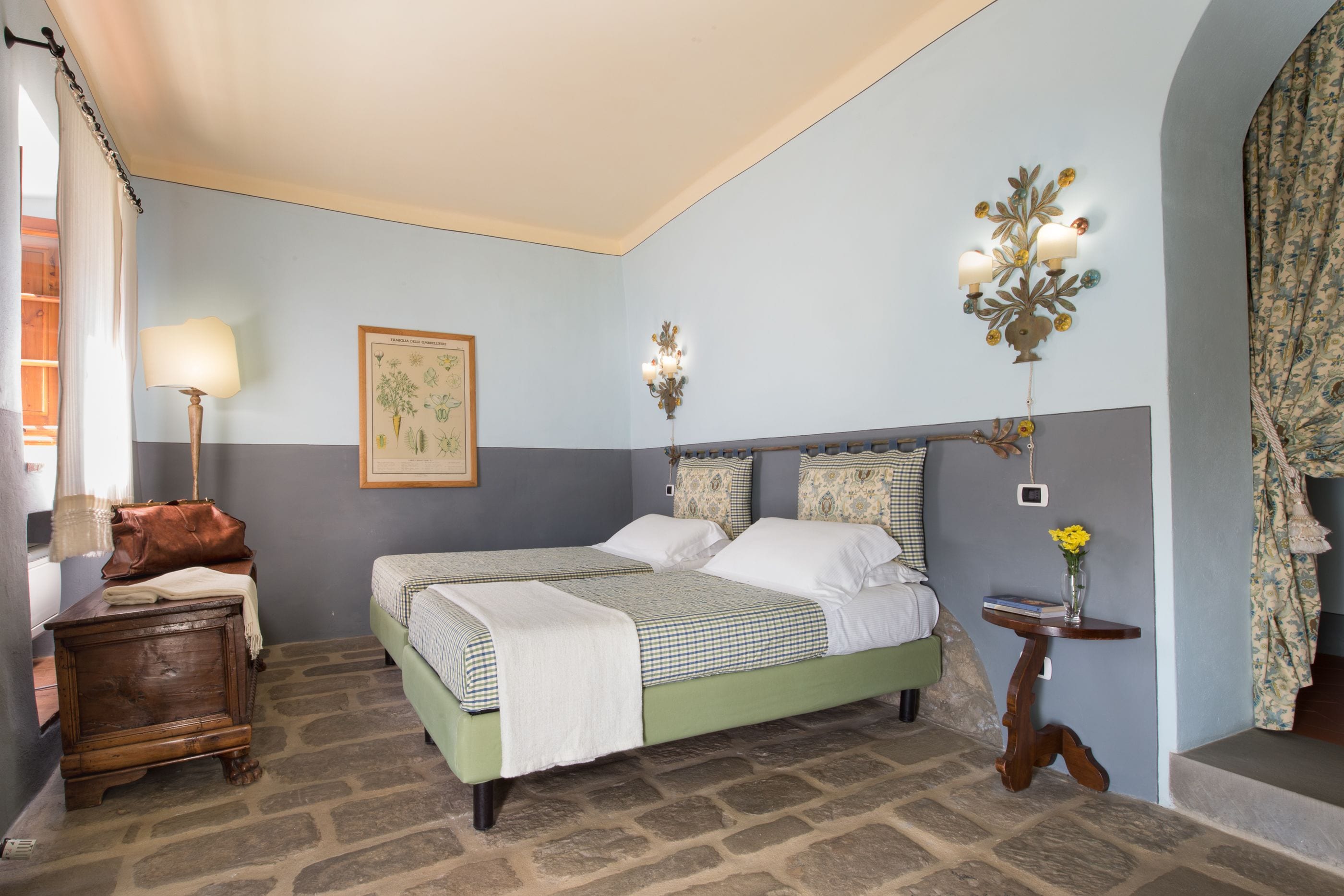 Une chambre à coucher avec un lit double, une table de chevet, une lampe, un luminaire fixé au mur et une petite table sur laquelle se trouve un vase.