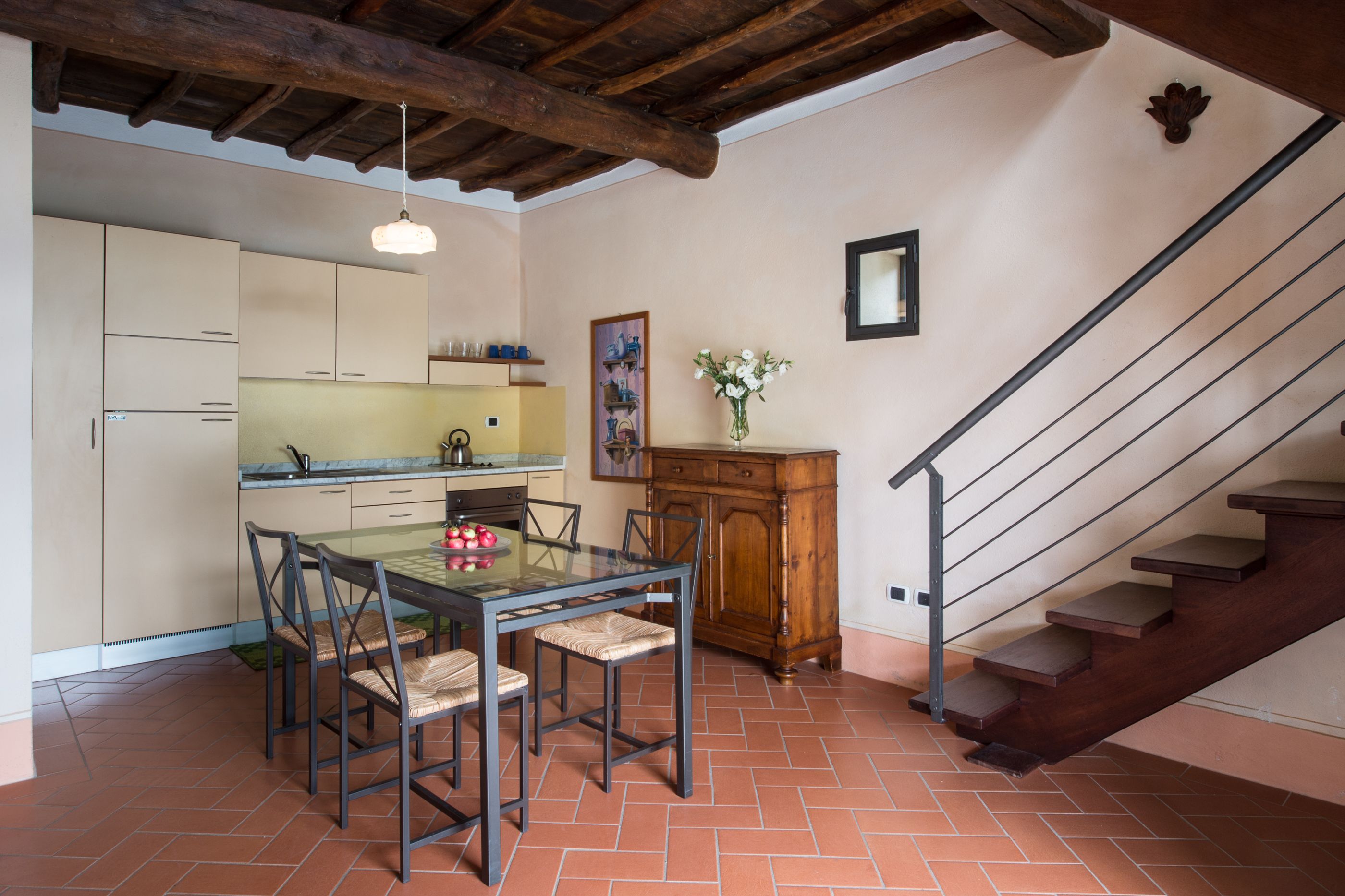 A kitchen with a dining table and chairs, a wooden cabinet, and a staircase.