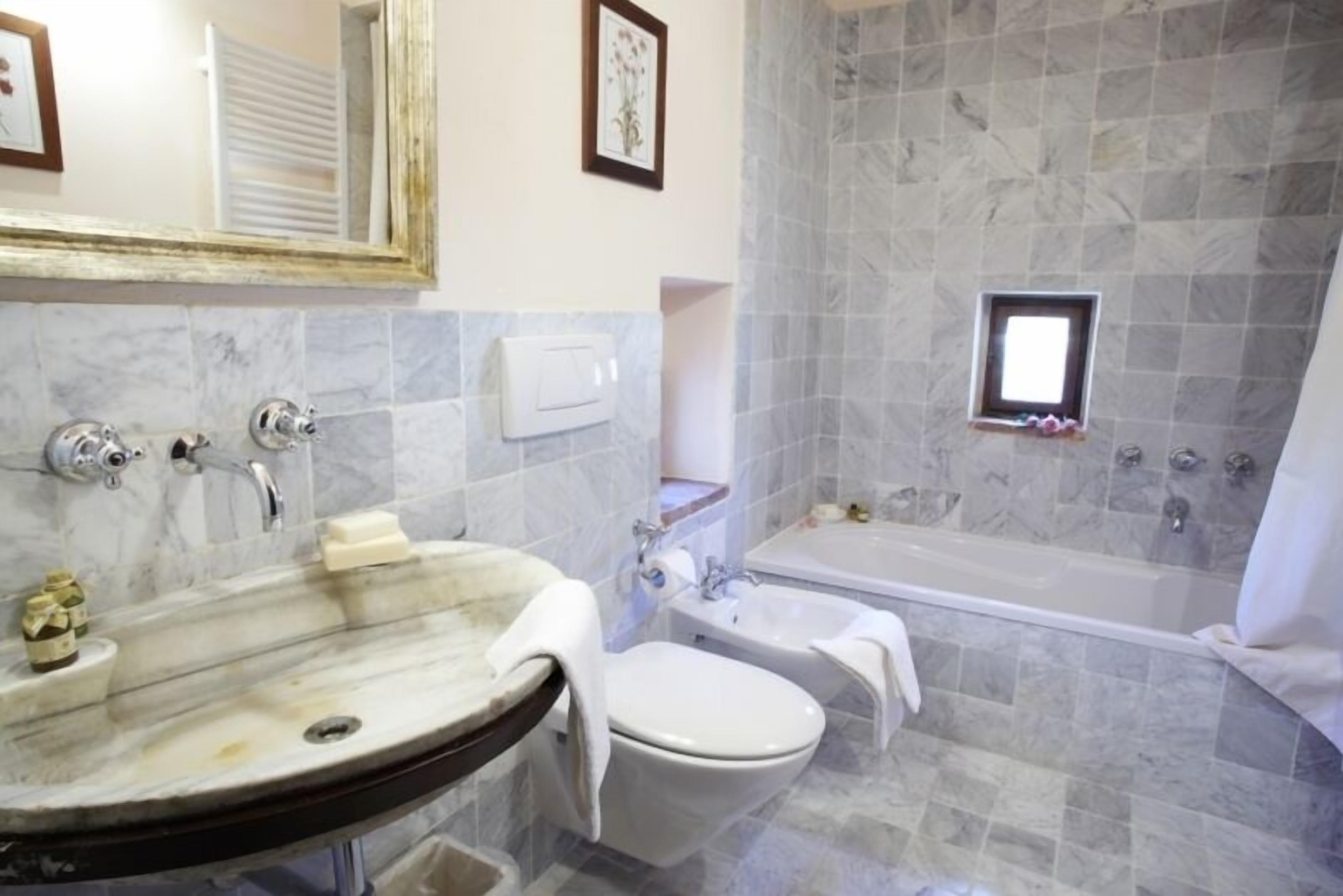 Une salle de bain avec un lavabo en marbre, des toilettes, une baignoire et une petite fenêtre.