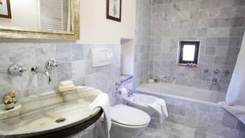 Une salle de bain avec un lavabo en marbre, des toilettes, une baignoire et une petite fenêtre.