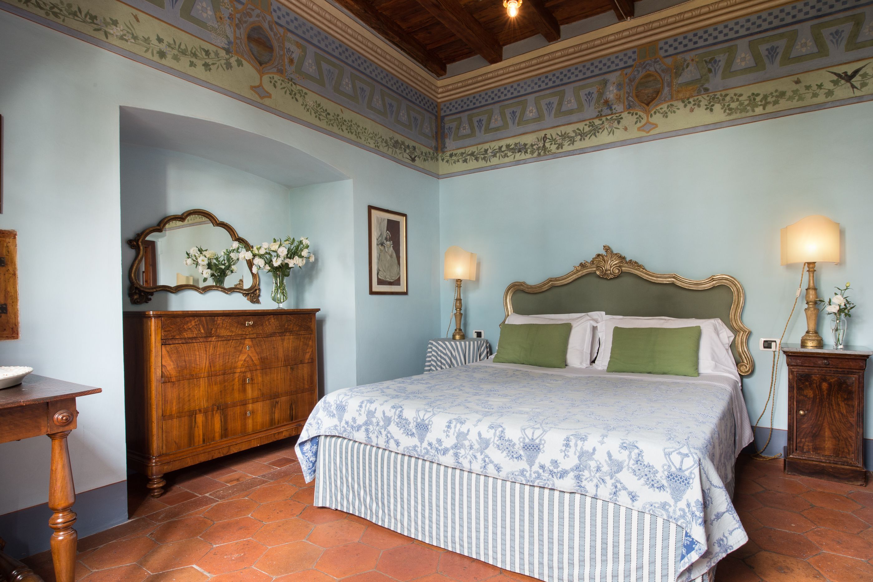A bedroom with a large bed, wooden dresser, and two bedside tables with lamps.