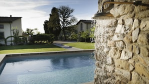 A swimming pool with a stone wall and a metal fixture on the right. - Relais Villa Belpoggio - Residenza d'Epoca (Loro Ciuffenna)