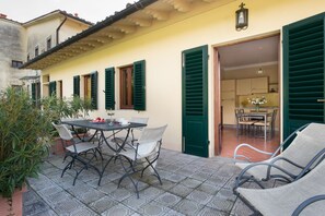 An outdoor patio with a table and chairs, a green door leading to a kitchen, and a tiled floor. - Relais Villa Belpoggio - Residenza d'Epoca (Loro Ciuffenna)