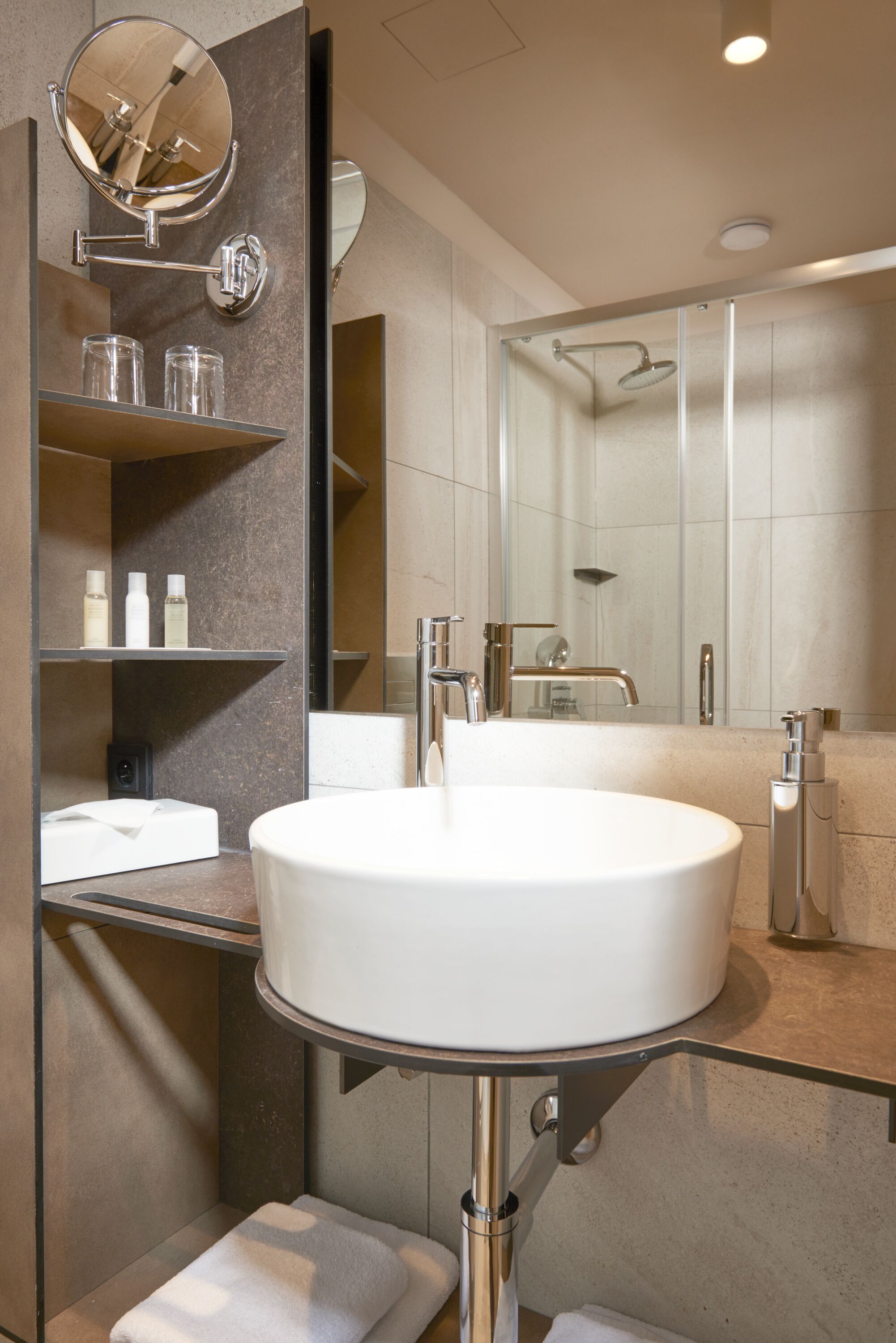 Un baño moderno con un lavabo redondo grande, un cabezal de ducha manual y un espejo sobre el lavabo.