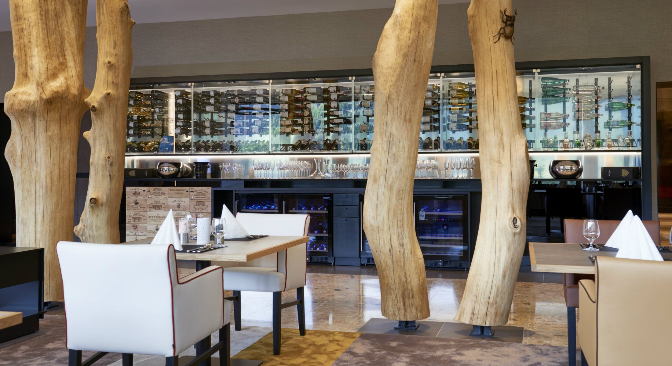 A restaurant interior with wooden pillars, tables, chairs, and a wine display.
