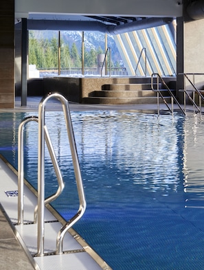 A swimming pool with metal railings, a view of trees and mountains through large windows, and a modern architectural design.
