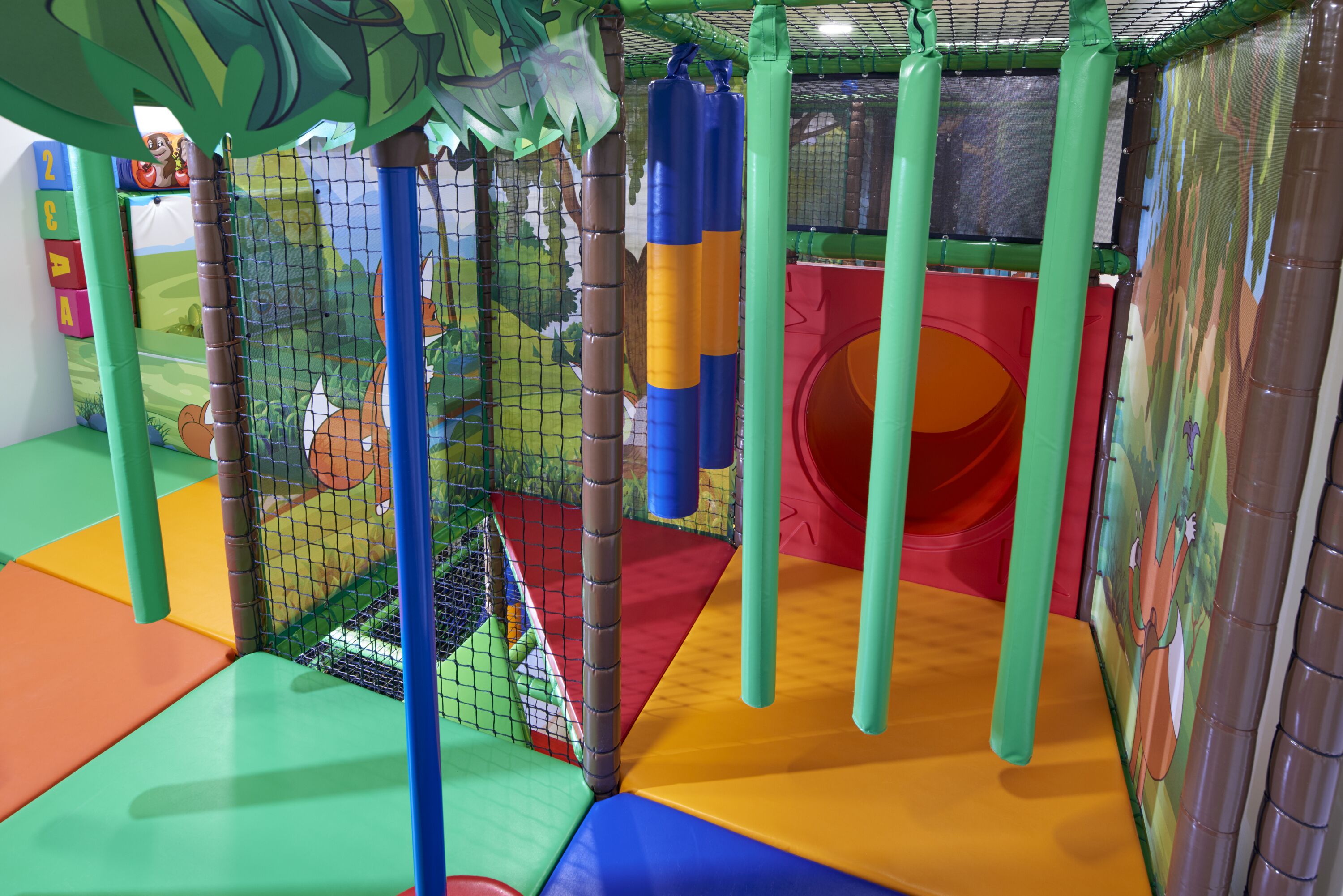 A play area with colorful padded flooring, netted play structures, and a slide.