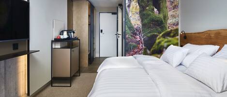 A hotel room with a bed, a desk with a coffee maker, a TV, and a door leading to another room.