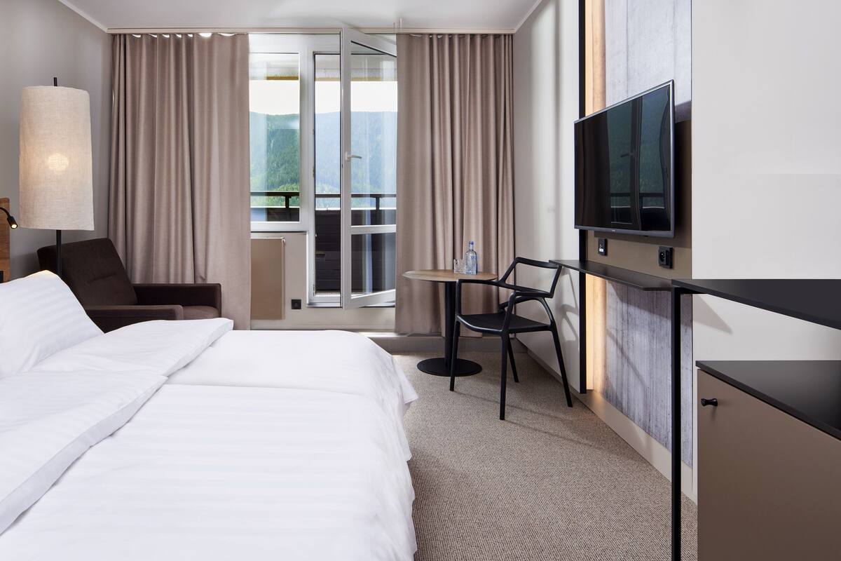 A hotel room with a large bed, a desk with a chair, a television, and a view of the outdoors through a sliding door.