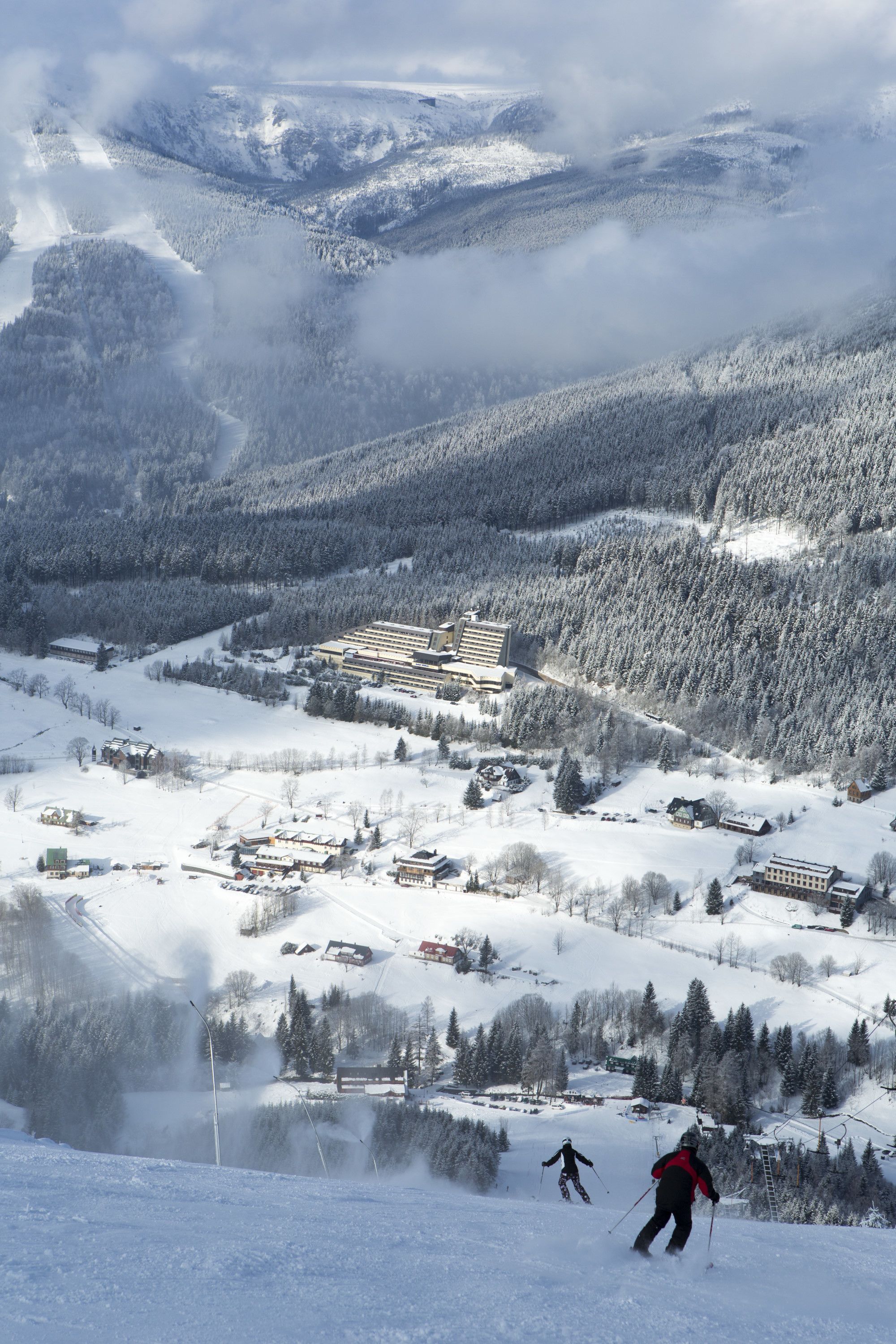A snow-covered mountain landscape with a ski resort, including buildings and ski slopes.