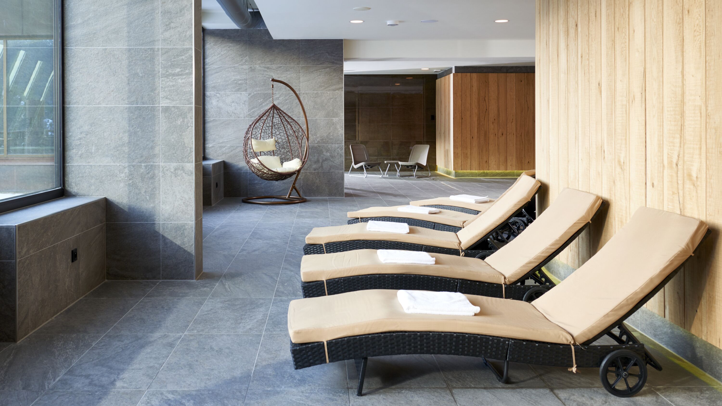 Zona de spa con sillones reclinables, una silla colgante y una pared de madera.