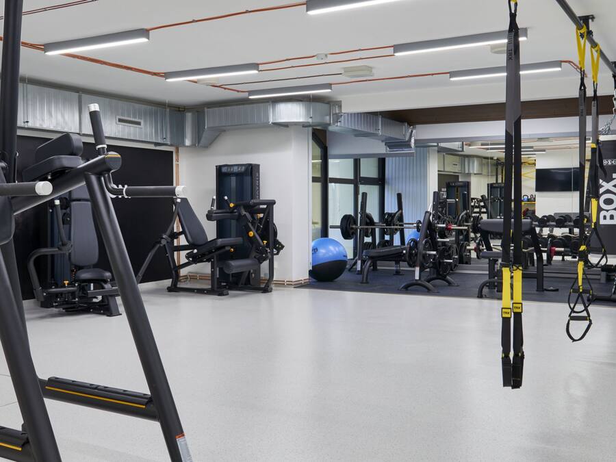Un gimnasio con diverso equipo de ejercicio, incluyendo cintas de correr, máquinas de pesas y aparatos de entrenamiento con suspensión.