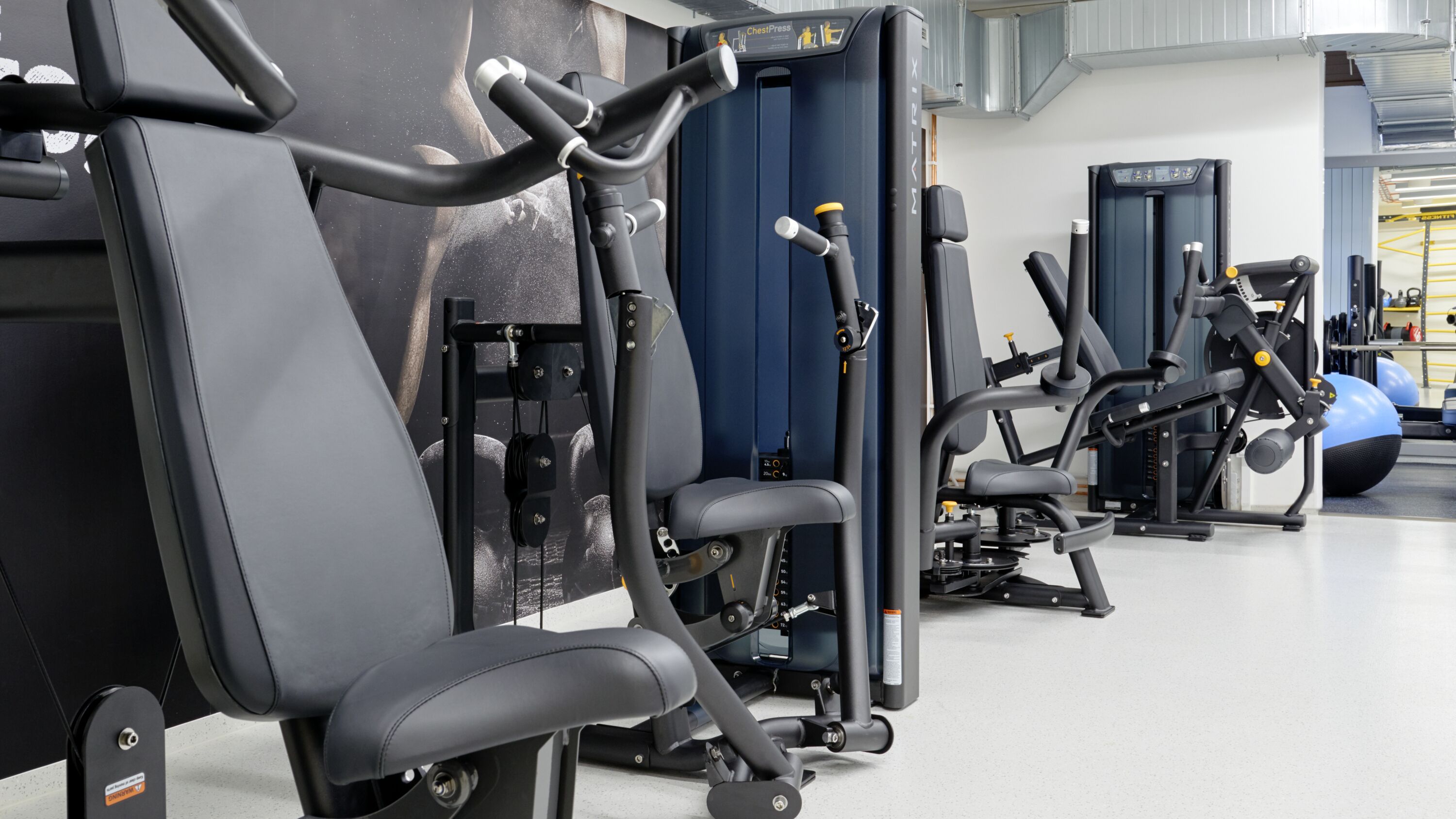 A gym with various exercise machines, including treadmills and weight machines, arranged in a spacious layout.