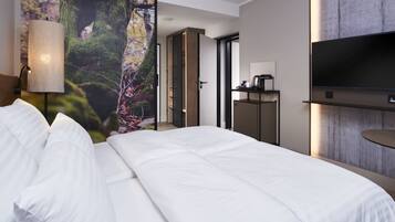 Una habitación de hotel moderna con una cama grande, un televisor montado en la pared y vistas a un bosque a través de un ventanal.