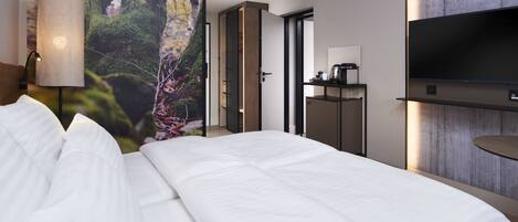 Una habitación de hotel moderna con una cama grande, un televisor montado en la pared y vistas a un bosque a través de un ventanal.