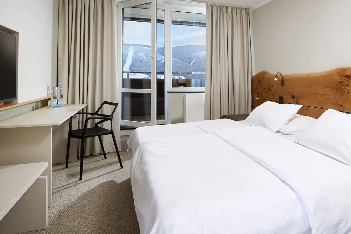 A hotel room with a bed, a desk, a chair, and a television.