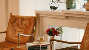 A room with two leather chairs, a wooden table with books and a glass of wine, and a vase with flowers. - Hôtel de Nell (Paris)