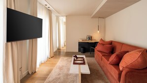 A modern living room with a flat-screen TV, a sofa, a coffee table, and a desk area. - Hôtel de Nell (Paris)
