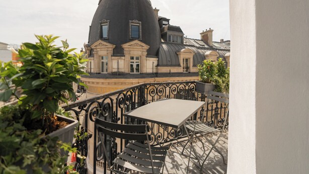 A balcony with a table and chairs, overlooking a building with a distinctive dome roof. - Hôtel de Nell (Paris)