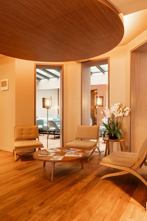 A modern interior with wooden flooring, a round coffee table with magazines, two armchairs, and a lounge chair. - Hôtel de Nell (Paris)