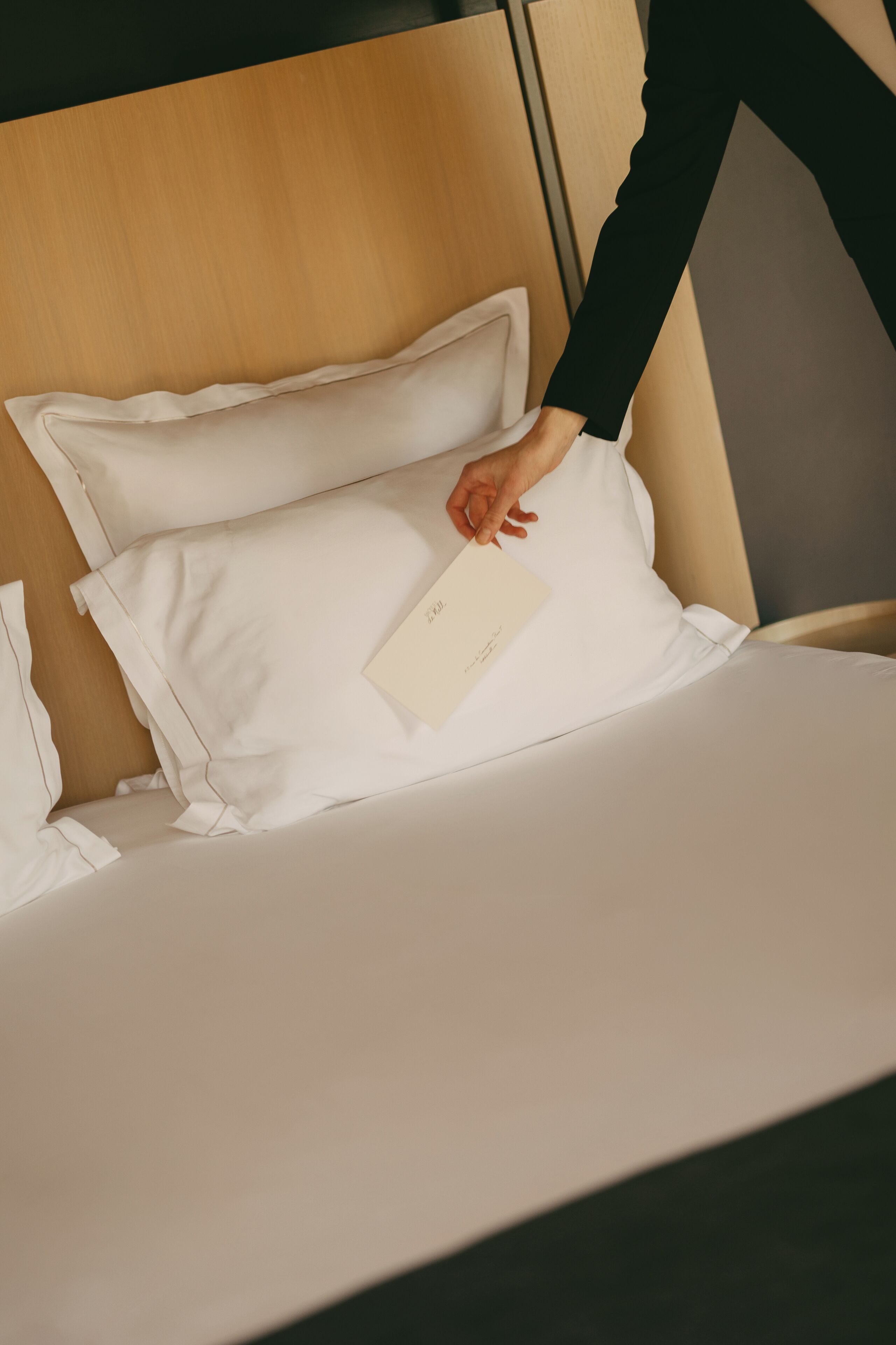 A hand adjusting a white pillow on a bed with a wooden headboard.