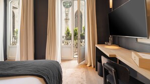 A hotel room with a bed, a desk, a TV, and a balcony with curtains. - Hôtel de Nell (Paris)